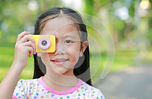 Portrait of smiling little girl takes photo with digital camera toy in the garden outdoor