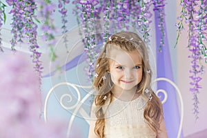 Portrait of smiling little girl in a yellow dress in a room decorated a lilacs