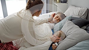 Portrait of smiling loving mother covering with blanket and looking at her children sleeping in bed. Concept of family happiness,