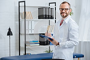 portrait of smiling male chiropractor in white coat and eyeglasses with notepad