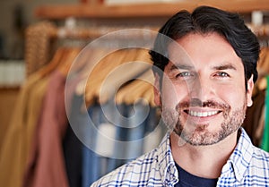 Portrait Of Smiling Male Owner Of Fashion Store Standing In Front Of Clothing On Rails