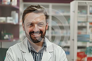 Portrait of smiling male pharmacist in white coat standing on pharmacy background
