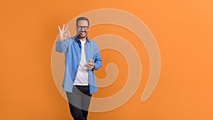 Portrait of smiling male professional using mobile phone and showing OK sign over orange background