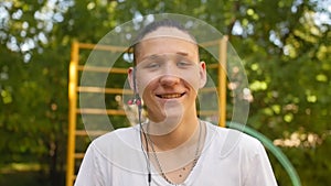 Portrait of smiling male teenager with headphone looking into the camera outdoors. Close up shot.