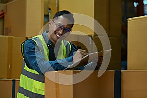 Portrait of smiling male warehouse worker in yellow vest checking papers on his clipboard. Distribution center and