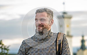 Portrait of a smiling man with a beard of 35-40 years old with a backpack on his shoulder against a blurry background of old archi