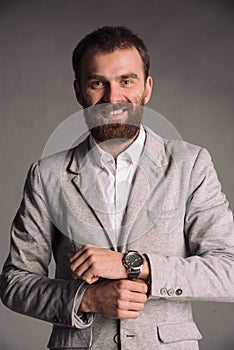 Portrait of smiling man with beard in white shirt and grey jacket isolated on gray studio background posing to the camera