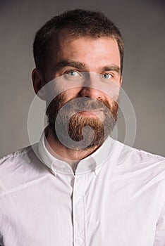 Portrait of smiling man with beard in white shirt isolated on gray studio background posing to the camera