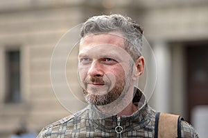 Portrait of a smiling man with a beard of 35-40 years old with a backpack on his shoulder against a blurry background of old archi