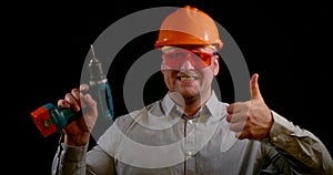 Portrait of a smiling man on a black background, he is wearing an construction helmet, safety glasses and a shirt, he is