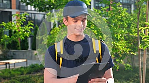 Portrait smiling man courier food delivery with thermal backpack uses tablet