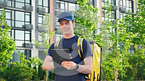 Portrait smiling man courier food delivery with thermal backpack uses tablet