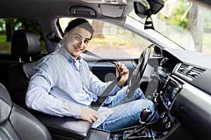 Portrait of smiling man fastening seat belt and sitting in his car
