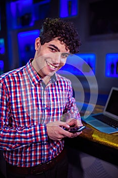 Portrait of smiling man holding mobile phone by bar counter