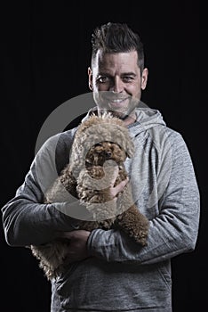 Portrait of a smiling man looking at the camera with a small red poodle dog. Black background. Vertical