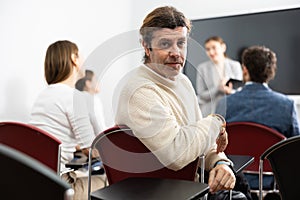 Portrait of smiling man participating in psychological trainings while sitting near employees in classroom