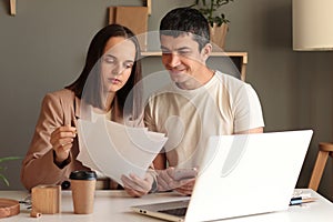 Portrait of smiling man and serious concentrated woman sitting at table together in front of laptop working together, female