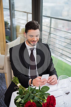 portrait of smiling man in suit using smartphone while waiting for girlfriend