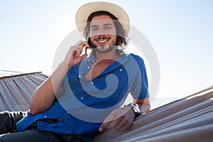 Portrait of smiling man talking on mobile phone while relaxing at beach
