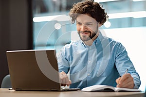 Portrait of smiling man using laptop and writing in notebook