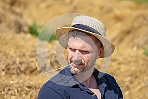 Portrait of a smiling man 35-40 years old with a beard in a straw hat on a field with hay. Concept: farming and agriculture, summe