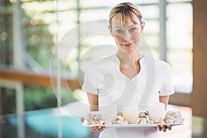 Portrait of smiling masseur holding tray with pebbles and candles