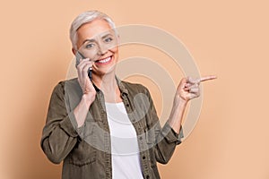 Portrait of smiling mature age business woman talk phone call with partner point finger copyspace proposition over beige