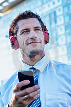 Portrait of smiling mature businessman listening to music on his smartphone with headphones on