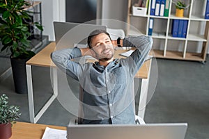 Portrait of smiling mature businessman relaxing on chair at workplace and dreaming, holding hands behind head