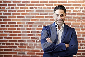 Portrait Of Smiling Mature Businessman Standing Against Brick Wall In Modern Office