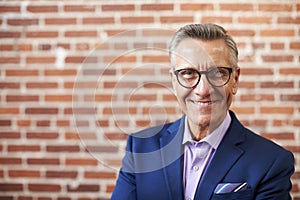 Portrait Of Smiling Mature Businessman Standing Against Brick Wall In Modern Office