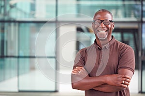 Portrait Of Smiling Mature Businessman Standing In Lobby Of Busy Modern Office