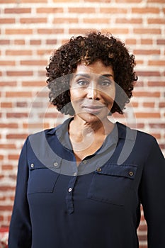 Portrait Of Smiling Mature Businesswoman Standing Against Brick Wall In Modern Office