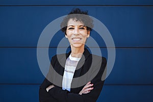 Portrait of smiling mature businesswoman standing arms crossed against blue wall