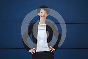 Portrait of smiling mature businesswoman standing with hands on hip against blue wall