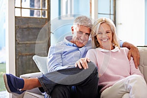 Portrait Of Smiling Mature Couple Sitting On Sofa At Home