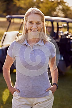 Portrait Of Smiling Mature Female Golfer Standing By Buggy On Golf Course