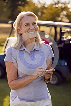 Portrait Of Smiling Mature Female Golfer Standing By Buggy On Golf Course With Score Card