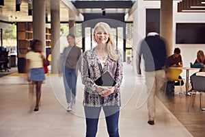 Portrait Of Smiling Mature Female Tutor In Busy University Or College Building With Students