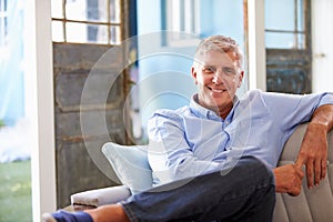 Portrait Of Smiling Mature Man Sitting On Sofa At Home