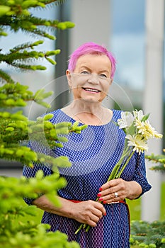 Portrait of smiling mature woman standing near fir-tree with spring flowers