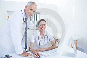 Portrait of smiling medical colleagues working with computer and looking at camera