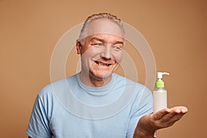 Portrait of smiling middle aged, 45s man holding jar of skin care hand cream, lotion, serum against beige background.