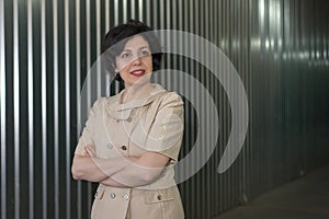 Portrait of smiling middle aged business woman with crossed arms on a container metal striped wall with light reflections.