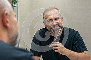 Portrait of smiling Middle-aged handsome man cutting his beard with scissors. Selfcare during quarantine isolation