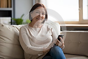 Portrait of smiling middle aged lady resting on sofa.