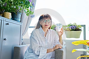 Portrait of smiling middle-aged woman with glass of water, at home