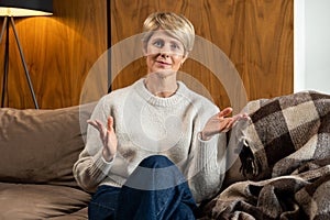 Portrait of a smiling middle-aged woman sitting on the sofa in the living room and looking at the camera. A happy lady