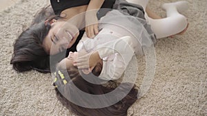 Portrait of a smiling Middle Eastern young woman playing with her daughter at the soft carpet. Happy mother spending