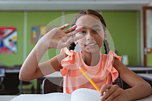 Portrait of smiling mixed race schoolgirl sitting at desk in classroom raising hand